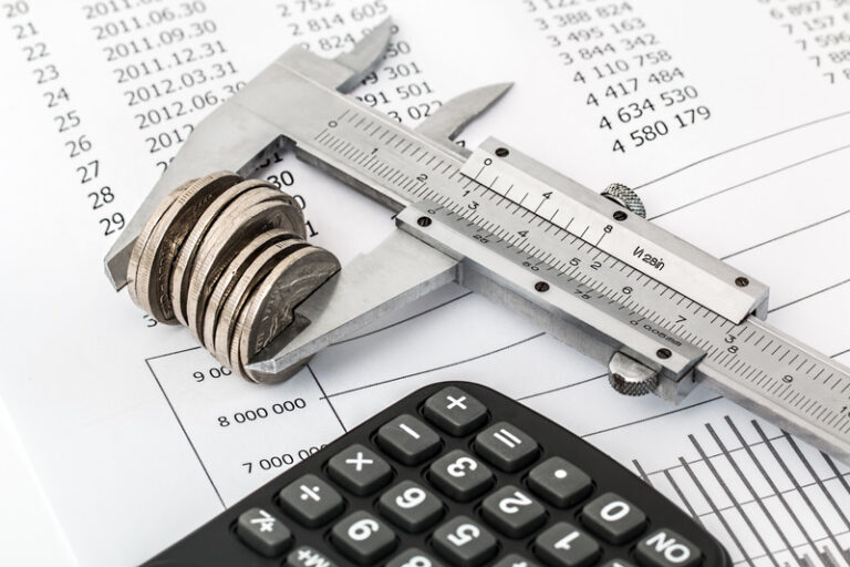 Measuring calipers holding coins next to calculator
